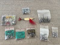 Assorted fishing accessories laid out, including multiple small plastic bags of weights and a plastic box with various weights and hooks.