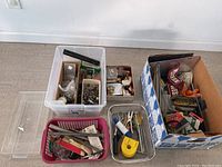Overview of multiple storage bins and baskets containing small hardware, tools, and fasteners in a garage setting.