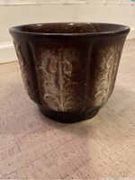 Oblique view of the brown jardiniere planter showing embossed floral pattern and tapered shape.