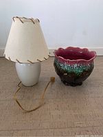 Photo showing both the white lamp with beige shade and the green and pink jardiniere placed side by side on the floor.