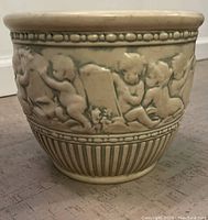 Front angle showing detailed cherub and floral raised relief design on ivory jardiniere