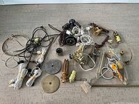 Overview of assorted lamp repair parts including cords, metal bases, sockets, harp frames, and other components arranged on floor