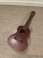 Full view of Lanikai LU-21T ukulele laying on floor showing wooden body and four strings.
