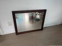 Front view of large rectangular mirror with dark wooden frame leaning against the wall