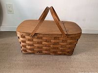 Front view of large wicker picnic basket showing woven wicker base, wooden lid, and two wooden handles upright.