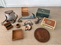 Overview photo showing all 12 miscellaneous trinkets arranged on floor: metal container, wooden boxes, decorative plaques, hanging sign, and small figurines.
