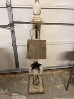 Front view of rustic wooden outdoor lantern with star cutout on the front panel, wires visible, set on square base.