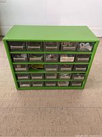 Front view of a small green garage organizer showing 30 transparent drawers containing various small parts and accessories.