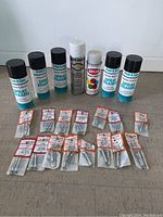 Spray enamel paint cans and multiple packages of metal wall anchors laid out on floor.