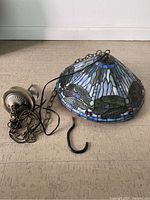 Full view of Tiffany style stained glass dragonfly pendant light laid on floor showing shade, chain, wiring, canopy and hook.