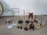 Various display stands including metal easels, small brass easels, wooden carved easels and bases, a glass dome with wooden base and a clear acrylic display case.