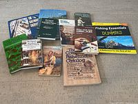 Full lot view showing 10 vintage fishing books on a concrete floor, including titles on saltwater and freshwater fishing, lures, and fishing essentials.
