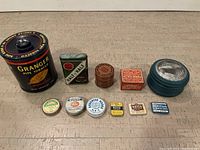 Overview of 11 vintage tins of various sizes and brands, arranged on floor