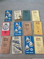 Lot photo showing 11 vintage railroad time logging books arranged on a flat surface, featuring multiple editions of 'Time Book' with different colors and cover designs.