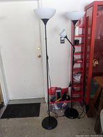 Full view of two black metal floor lamps with white glass shades set next to each other near a door and red shelving unit.