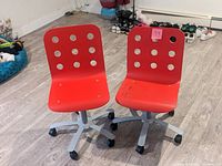 Front view of two red low chairs on metal caster bases, showing circular holes in the backrest, one chair with visible stains.