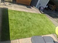 Full view of rectangular artificial turf carpet laid out on pavement, showing green synthetic grass fiber surface.