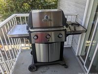 Front view of Broil King BBQ grill showing stainless steel lid, three control knobs, and mounted on wheeled cart.