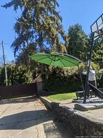 Folding green sun shade umbrella set up outdoors showing canopy and curved arm pole.