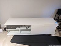Front view of white lacquer low console cabinet showing closed glass doors, open shelving below, and chrome base.