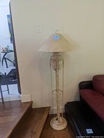 Full view of vintage metal floor lamp standing next to a brown couch and a staircase, showing its height and overall design