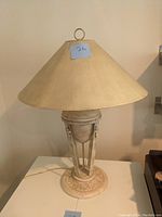 Full view of vintage metal table lamp with cream lampshade and ornate metal base highlighting aged patina and distressed finish.