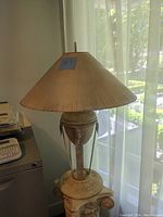 Full view of the vintage metal table lamp showing its conical fabric shade and overall shape by a window with natural light.