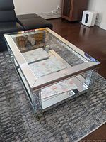 Overall view of the rectangular mirror and chrome coffee table on a patterned area rug in a living room setting showing the reflective mirrored top and chrome frame.