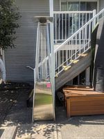 Full view of outdoor stainless steel pyramid patio heater showing metal base, mesh protective cage, and top reflector.