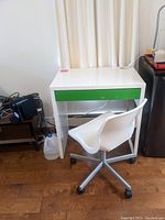 Small white desk with single green drawer, and white office chair with wheels beside it, showing overall appearance and condition of furniture items.