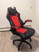Front side view of the Staples Luxera gaming chair showing red and black upholstery, cushioned armrests, and seat padding.