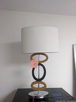 Front view of the vintage table lamp showing the white drum shade and three oval metal accent rings on the lamp body, with the chrome circular base.