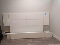 Full view of disassembled white lacquer queen bed frame components leaning against a wall, including headboard, footboard and side rails.