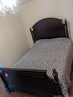 Full view of dark wooden queen bed frame showing footboard and mattress with printed cover in a room with chandelier
