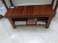 Angled view of wooden shoe rack bench showing top surface and two lower shelves with stored magazines.