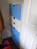 Side view of tall wooden storage unit with five closed drawers, alternating blue and white