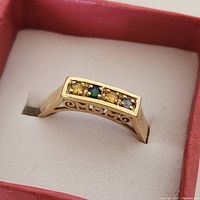 Close-up photo of the yellow gold ring showing all four birthstones and the MOM cut-out on the side.