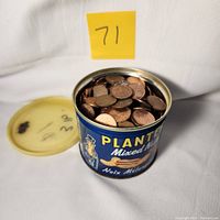 A vintage Planters Mixed Nuts tin filled with pennies, lid removed and placed behind, with a numbered yellow post-it note '71'.