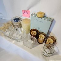Overview of glass votive holders, wax pillar candle, battery votive candles, and partial tea light box.