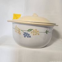 Stoneware casserole dish with lid, white base and floral pattern of yellow and blue flowers with green leaves on the side, lid and interior are creamy yellow.