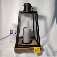 Front view of large candle lantern showing wooden base, glass panels, metal frame, and grey battery operated candle inside with a water bottle for size reference.