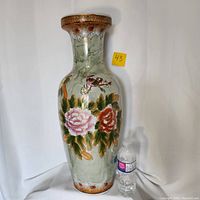 Front view of a tall floor vase showing its shape and primary floral and bird decorations beside a water bottle for scale.