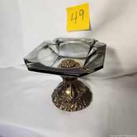 Clear image showing full ashtray from front, highlighting square smoked glass top and decorative metal pedestal base.