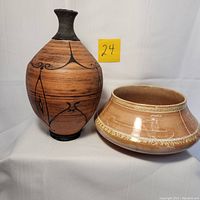 Photo showing both pottery pieces, vase with black details and bowl with white designs, against plain backdrop