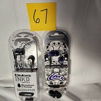 Two sets of Skullcandy ear buds in packaging, one black and one purple, with labels indicating compatibility and microphone.