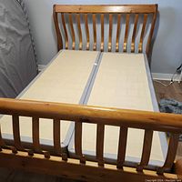 View of assembled queen size sleigh bed frame with split boxspring set inside showing curved slat headboard and footboard in pine wood finish.