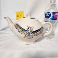 Front view of cream ceramic teapot with colorful native thunderbird design, yellow sticky tag 63 and Pure Life water bottle for scale