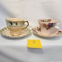 Two vintage teacup and saucer sets side by side, showing front view including colors and gold trim detail.