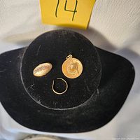Photo of the lot including the 14K gold sombrero charm, child's broken ring, and antique monogrammed tie clip on black velvet display.