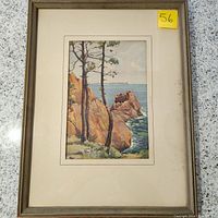 Full view of framed and matted chromolithograph showing a coastal scene with rocky shoreline and two trees, with visible wear on frame and matting.